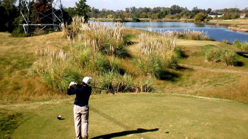A player on the tee with pampas grass and water in play